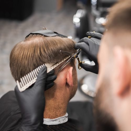 Hairdresser scissors hair on the head sides for a stylish black-haired man in the barbershop